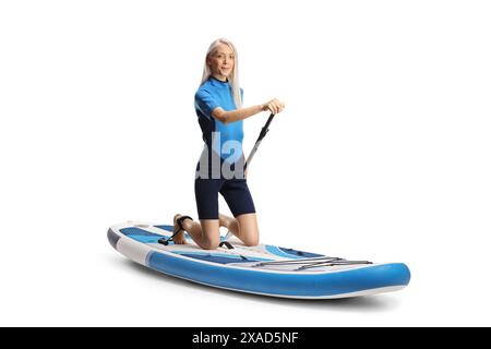 Femme dans une combinaison avec une pagaie agenouillée sur une planche de sup isolé sur fond blanc Banque D'Images