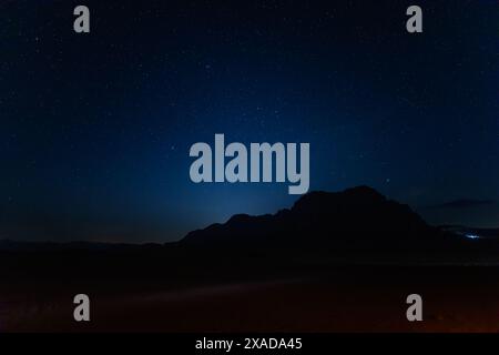 Un ciel nocturne captivant, parsemé d'étoiles, se couche sur la silhouette de la formation rocheuse Jabal al Qattar dans le paisible désert de Wadi Rum en Jordanie Banque D'Images