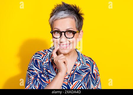 Photo de belle dame âgée toucher le menton pense porter chemise isolée sur fond de couleur jaune Banque D'Images