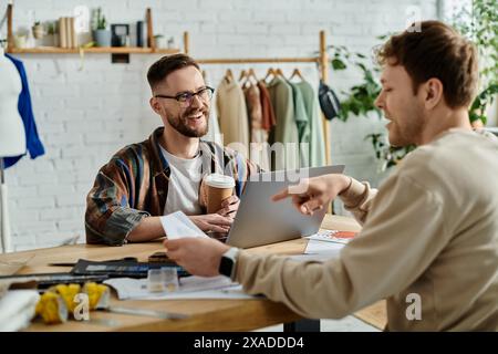 Deux hommes collaborent passionnément sur un ordinateur portable dans un atelier de designer. Banque D'Images