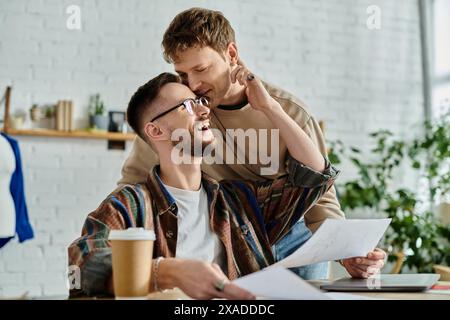 Deux hommes sont assis à une table, concentrés sur un papier rempli de dessins, dans un atelier de designer. Banque D'Images