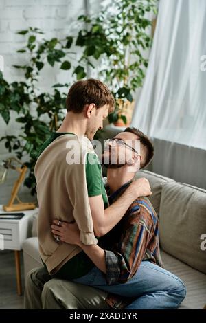 Deux hommes, faisant partie d'un couple gay, assis sur un canapé élégant dans un atelier de designer, serrés d'amour Banque D'Images