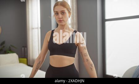 Une jeune femme confiante avec des tatouages se tient dans un intérieur de chambre, dégageant une féminité moderne et élégante. Banque D'Images