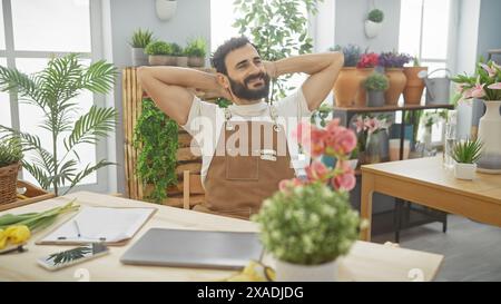 L'homme barbu détendu profite d'une pause dans un magasin de fleurs animé, entouré d'une végétation luxuriante et d'arrangements floraux. Banque D'Images