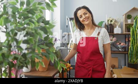 Femme hispanique souriante dans un tablier rouge disposant des tulipes à l'intérieur entouré de plantes d'intérieur Banque D'Images