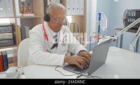 Un homme caucasien senior travaillant sur un ordinateur portable dans une clinique, peut-être un médecin ou un vétérinaire, portant des écouteurs et un manteau blanc avec un stéthoscope dans un puits-org Banque D'Images