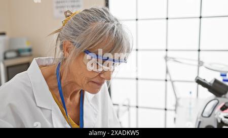 Femme mature avec les cheveux gris travaille concentré dans le laboratoire portant des lunettes de sécurité. Banque D'Images