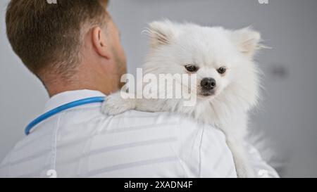 Vue arrière d'un jeune homme caucasien tenant son chien malade à l'intérieur à la clinique vétérinaire, alors que le vétérinaire professionnel en uniforme examine pour la santé i. Banque D'Images