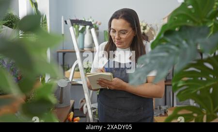 Une femme hispanique mature dans un magasin de fleurs prenant des notes avec des plantes qui l'entourent à l'intérieur. Banque D'Images