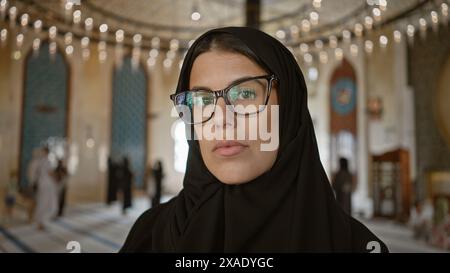 Une femme réfléchie dans un hijab posant à l'intérieur de la mosquée ornée de katara à doha, au qatar, mettant en valeur l'architecture culturelle et religieuse. Banque D'Images