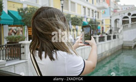 Une jeune femme prend une photo de l'architecture vénitienne vibrante sur son smartphone dans un élégant quartier qatari. Banque D'Images