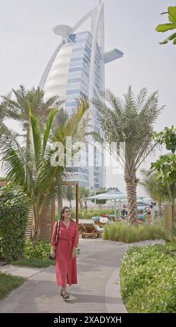 Une femme adulte se promène près de l'emblématique burj al arab de dubaï sous un ciel dégagé. Banque D'Images