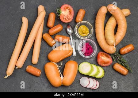 Saucisses de différentes variétés sur noir. Moutarde et raifort dans des bols en verre, brins de romarin et piment sur table. Pose à plat Banque D'Images