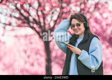 femme mélomane vérifiant des chansons sur son téléphone copie espace florissant sakura sur fond Banque D'Images