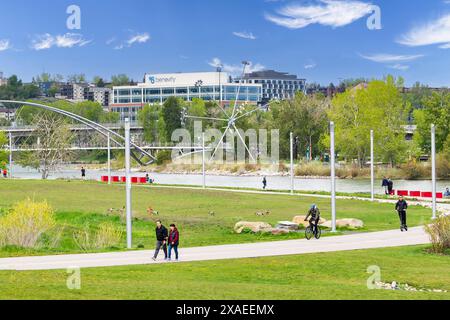 Calgary Alberta Canada, mai 30 2024 : piétons et cyclistes empruntant une passerelle le long d'une rivière surplombant un parc municipal à East Village. Banque D'Images