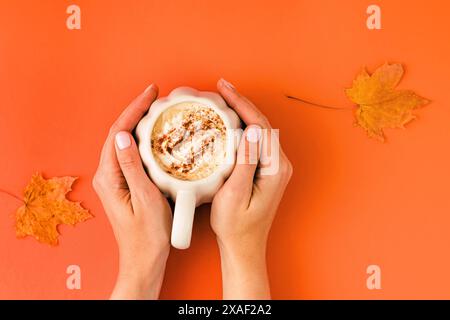 Femme tenant une tasse en forme de citrouille avec un latte aux épices d'automne ou une boisson saisonnière au chocolat chaud, vue de dessus Banque D'Images