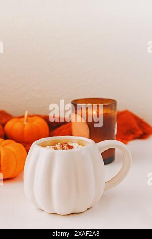 Composition d'automne confortable avec latte épicé dans une tasse en forme de citrouille surmontée de cannelle, de petites citrouilles décoratives et d'une bougie Banque D'Images