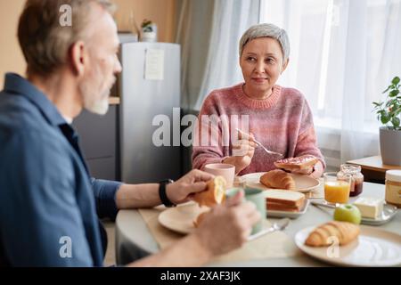 Portrait de femme senior asiatique appréciant le petit déjeuner à la table du dîner avec mari dans la cuisine confortable Banque D'Images
