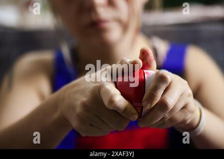 Un cliché précis capturant les mains d'une artiste féminine alors qu'elle presse habilement la peinture rouge d'un tube, soulignant son engagement dans le processus créatif. Banque D'Images