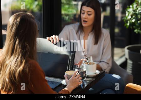 Deux jeunes femmes d'affaires dans un café ayant un sur une réunion. Amis après le travail parlant de gossiping et d'avoir le café à une table de fenêtre avec réflexion Banque D'Images