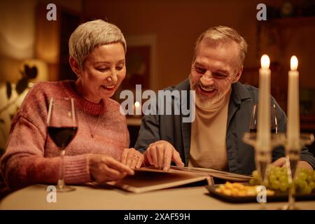 Portrait de couple senior souriant regardant l'album photo tout en profitant de la nuit romantique de date à la maison espace de copie Banque D'Images
