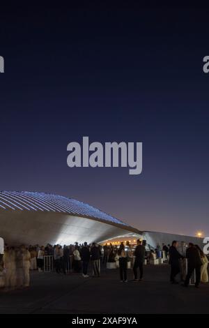 Un grand groupe de personnes profitant de la chaude nuit en dehors du centre. Siège social de BEEAH, Sharjah, Émirats arabes Unis. Architecte : Zaha Hadid architecte Banque D'Images