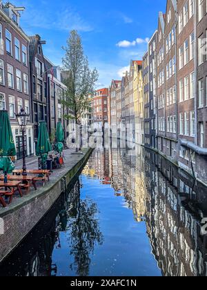 Bâtiments d'architecture hollandaise traditionnelle sur un canal d'Amsterdam. Réflexion des bâtiments sur l'eau. Terrasse sur le côté gauche. Banque D'Images