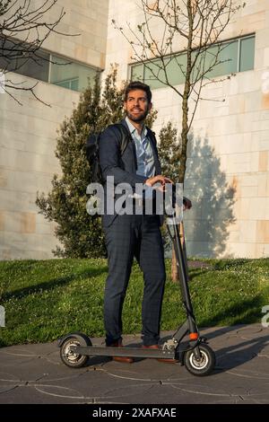 homme d'affaires vertical frappe une pose confiante avec son scooter électrique dans le quartier financier animé de la ville. Incarner l'éco-conscience an Banque D'Images