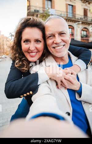 Vertical. couple mature sur une relation souriant et regardant la caméra. Femme adulte moyenne embrassant son mari de cheveux grai et se liant à l'extérieur. Des gens mariés d'âge moyen appréciant un câlin affectueux. Photo de haute qualité Banque D'Images