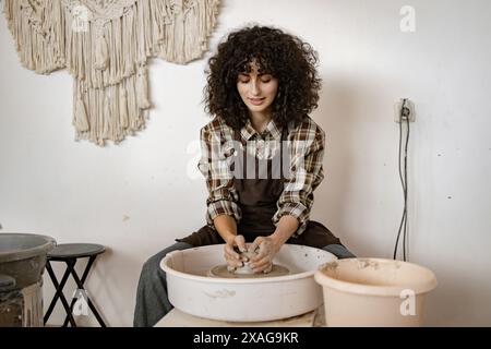 Potier féminin travaillant sur un plat en céramique à l'aide d'une roue de potier. Concentré et créatif dans un environnement de studio. Banque D'Images