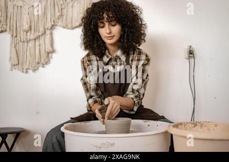 Jeune femme adulte travaillant sur le plat en céramique sur la roue du potier. Axé sur la création artisanale avec une ambiance détendue dans un studio de poterie. Banque D'Images