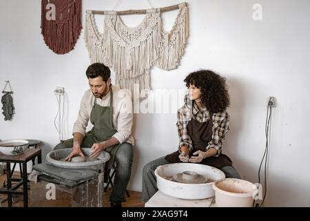 Potier homme et femme créant un vase en argile ensemble sur la roue du potier en studio. Artisanat fait à la main et travail d'équipe créatif dans un atelier de céramique. Banque D'Images