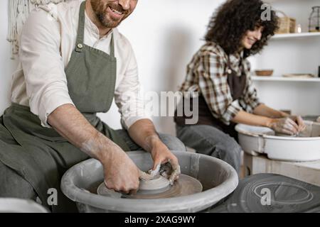 Homme et femme appréciant l'artisanat de poterie sur une roue de potier dans un cadre de studio créatif. Ils ont l'air heureux et engagés dans la création artistique. Banque D'Images