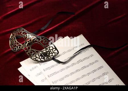 Masque facial élégant et feuilles de musique sur tissu rouge. Représentation théâtrale Banque D'Images