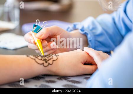 Une main de femme est ornée d'un tatouage au henné par une autre femme. L'artiste de henné applique soigneusement un design décoratif avec un cône rempli de HE Banque D'Images