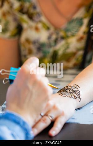 Une femme reçoit un tatouage au henné sur son poignet dans un salon. L'artiste applique soigneusement la pâte de henné avec un petit bâton, tandis que la femme regarde Banque D'Images