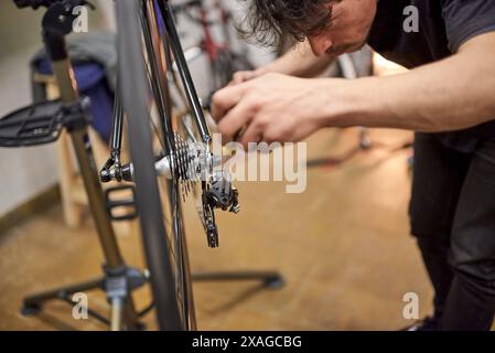 Réparateur en activité : un homme hispanique s'est concentré sur le réglage d'un dérailleur de bicyclette dans son atelier de réparation. De vraies personnes au travail. Banque D'Images