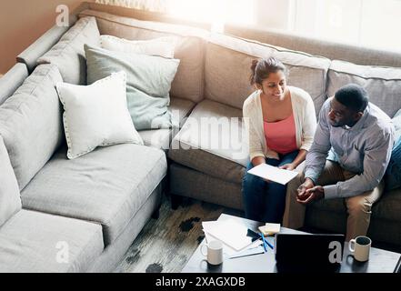 Lecture, couple et ordinateur portable sur canapé le matin pour le travail, les paiements et le loyer avec taxe dans le salon. Lumière du soleil, technologie et café avec les gens allumés Banque D'Images