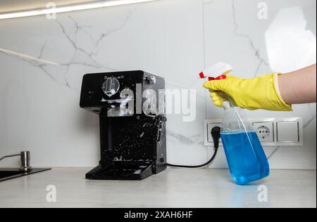 La jeune fille tient dans sa main un spray anti-graisse pour nettoyer la cuisine de la graisse et de la saleté. Lavage et nettoyage d'une machine à café et cuisine appli Banque D'Images