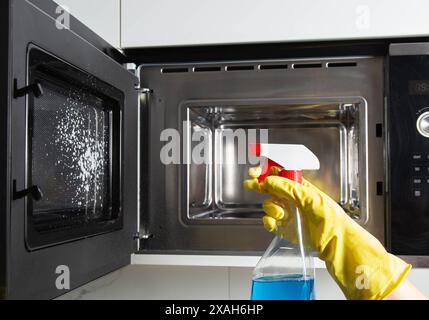Spray anti-graisse dans la main d'une fille qui nettoie la cuisine. Nettoyer le four à micro-ondes de la graisse et de la saleté. Agent antistatique moderne. Banque D'Images