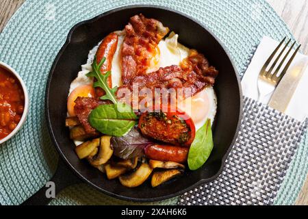 English petit déjeuner dans une poêle avec œufs frits, saucisses, bacon, champignons, haricots et tomates Banque D'Images