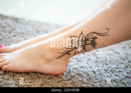 Une image en gros plan d'une femme chevilles, mettant en vedette un délicat tatouage floral au henné sur sa cheville droite. Le tatouage est complexe et détaillé, avec un grand f Banque D'Images