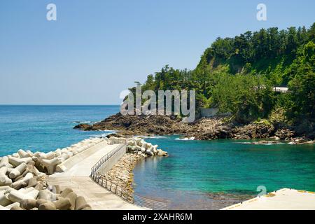 Samcheok City, Corée du Sud - 18 mai 2024 : la côte rocheuse et les eaux turquoises le long d'Isabu Road, avec un brise-lames protecteur. Le vert luxuriant h Banque D'Images