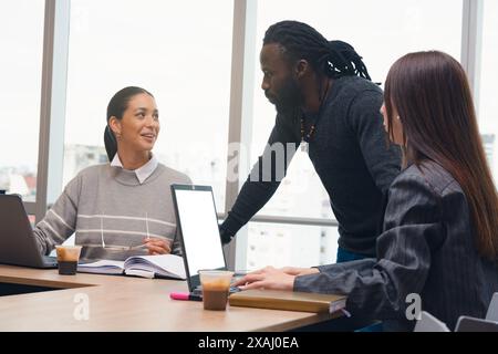 Trois personnes sont assises à une table dans une salle de conférence, travaillant sur un projet. L'homme au milieu donne des instructions à la femme à sa gauche. Banque D'Images