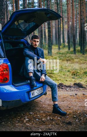 Hommes avec hommes bleus Mini Cooper Country et parapluie bleu le jour nuageux dans la forêt de pins. Banque D'Images