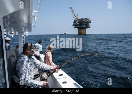 Un pêcheur à la ligne défile dans un thon capturé près de plates-formes pétrolières flottantes dans le golfe du Mexique, illustrant la juxtaposition de la pêche récréative et du pétrole au large Banque D'Images