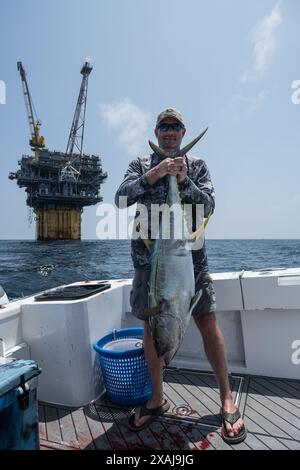 Un pêcheur à la ligne défile dans un thon capturé près de plates-formes pétrolières flottantes dans le golfe du Mexique, illustrant la juxtaposition de la pêche récréative et du pétrole au large Banque D'Images