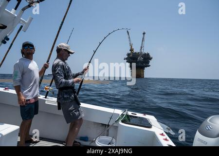 Un pêcheur à la ligne défile dans un thon capturé près de plates-formes pétrolières flottantes dans le golfe du Mexique, illustrant la juxtaposition de la pêche récréative et du pétrole au large Banque D'Images