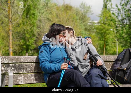 Amis non binaires s'embrassant assis dans un parc public. Banque D'Images