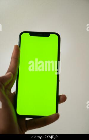 Une main tenant un téléphone intelligent avec un écran vert vif, isolé sur un fond clair. Banque D'Images